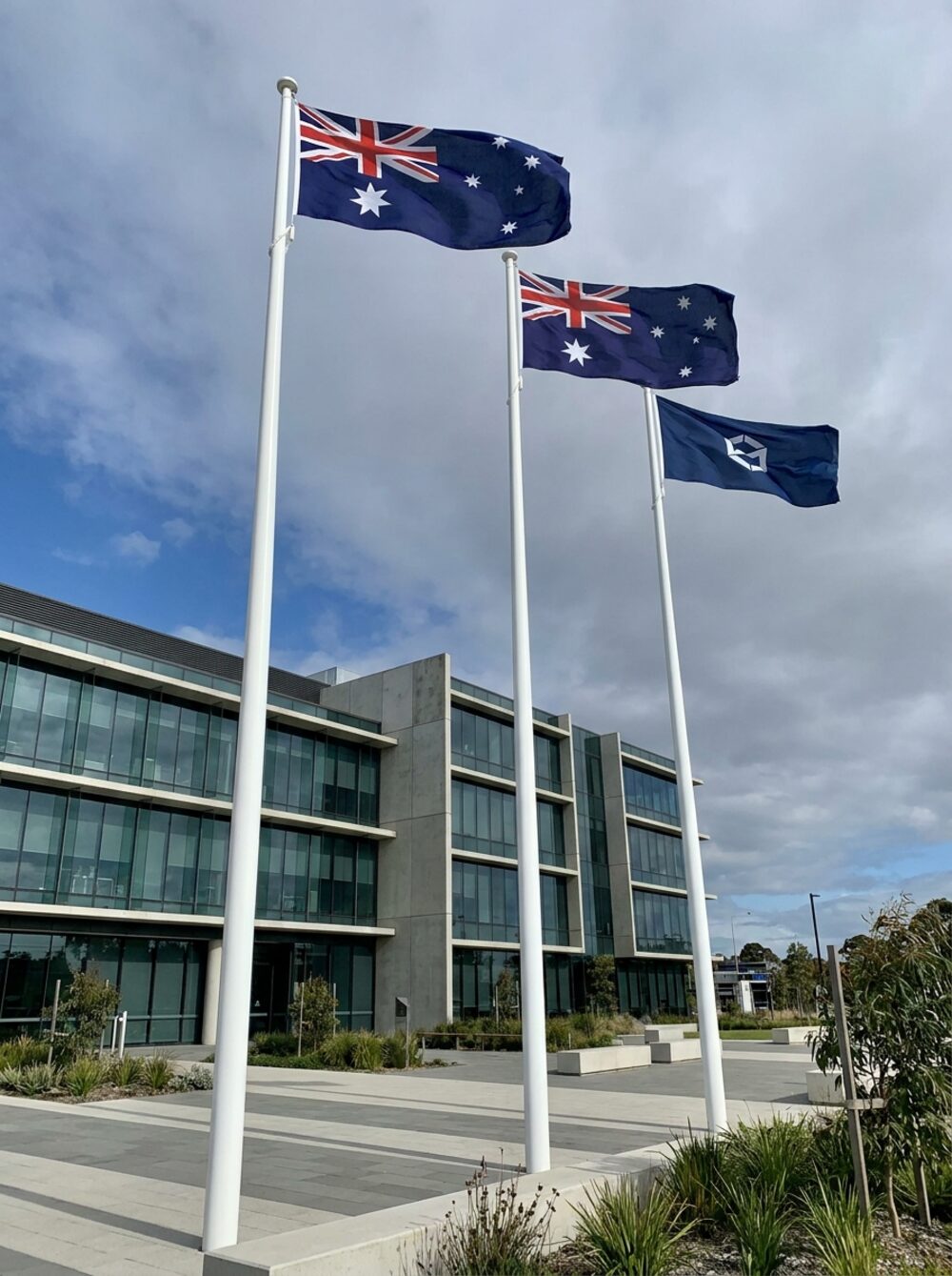 Three tall white commercial flagpoles outside a modern building