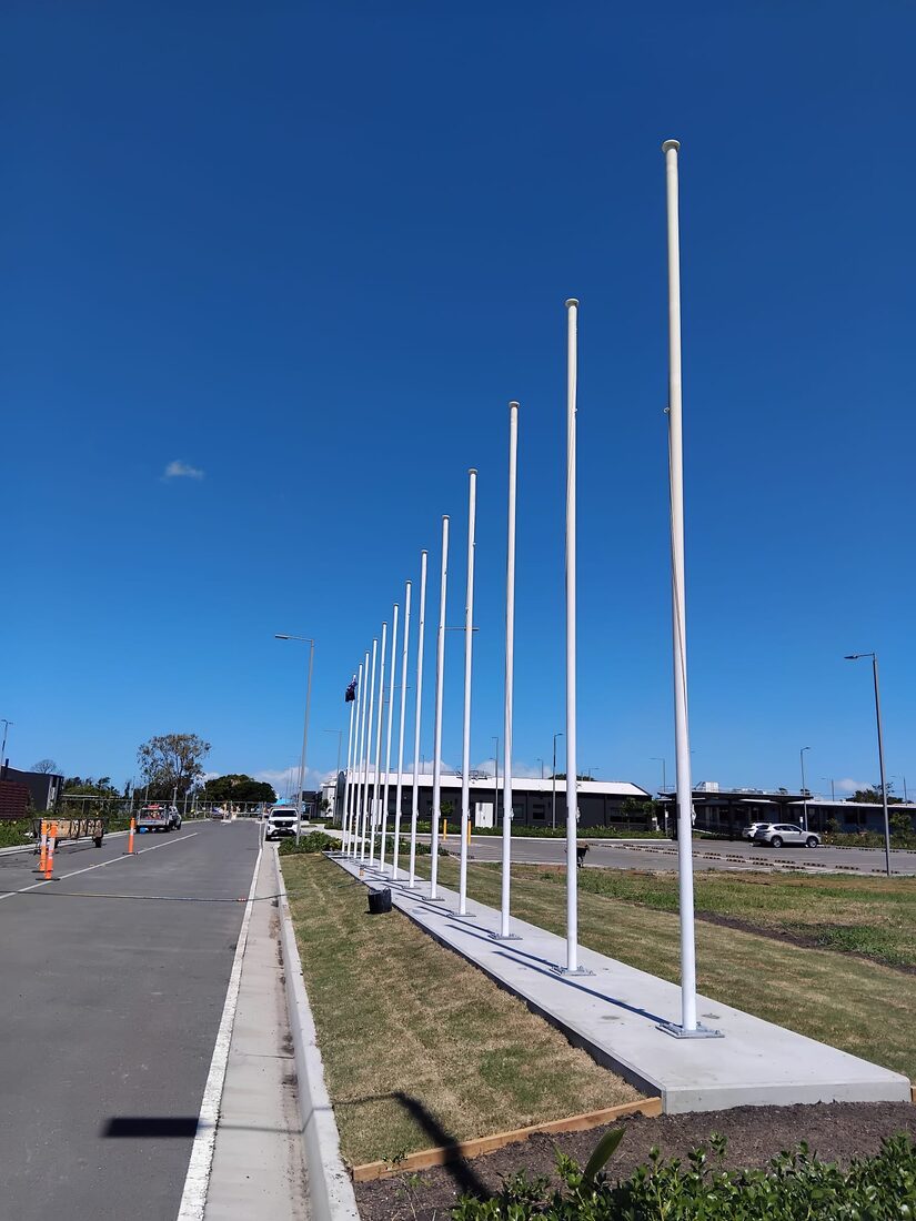 A long row of tall white flagpoles freshly installed beside a car park